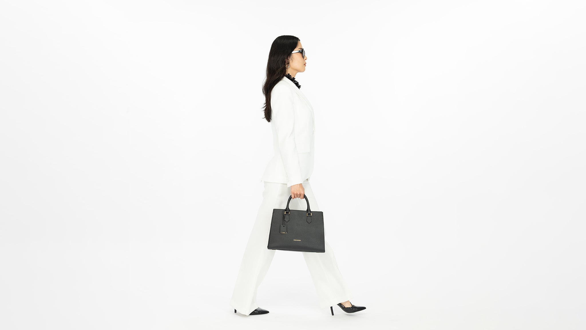 Stylish woman holding a black leather handbag against a clean white background
